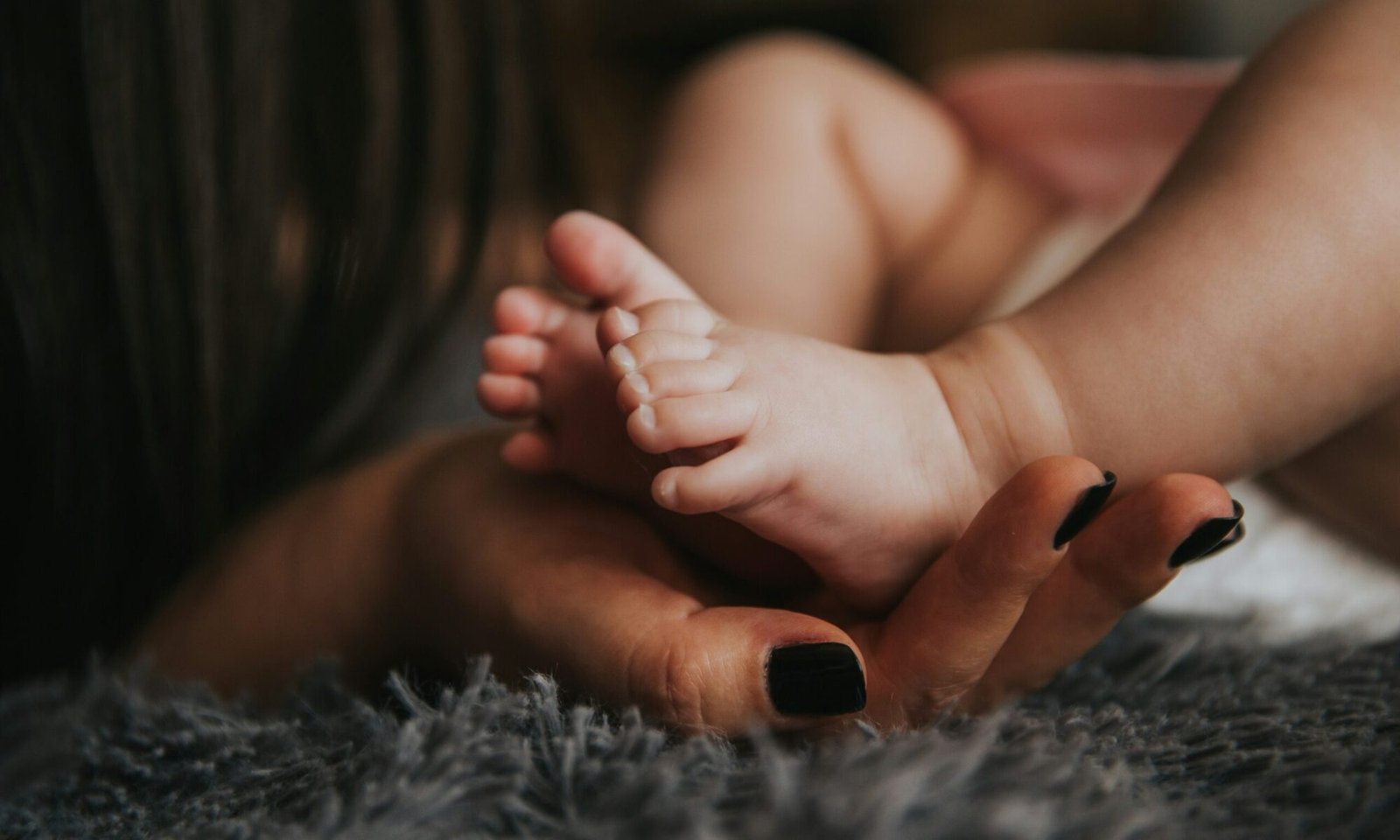 Woman’s hands gently holding a baby’s feet, symbolizing prenatal and postnatal care and maternal support.